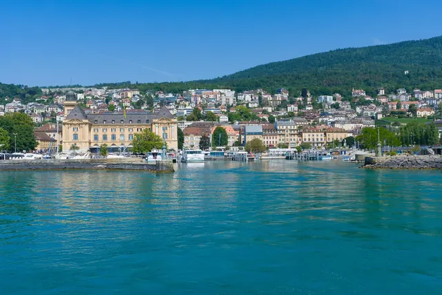 NeuchÃ¢telin satama, veneitÃ¤ ja rinnerakennuksia aurinkoisena pÃ¤ivÃ¤nÃ¤