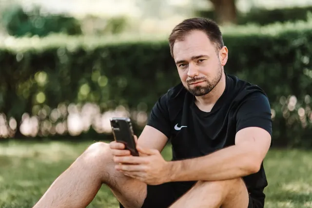 Mies istuu nurmikolla ja katsoo Ã¤lypuhelinta