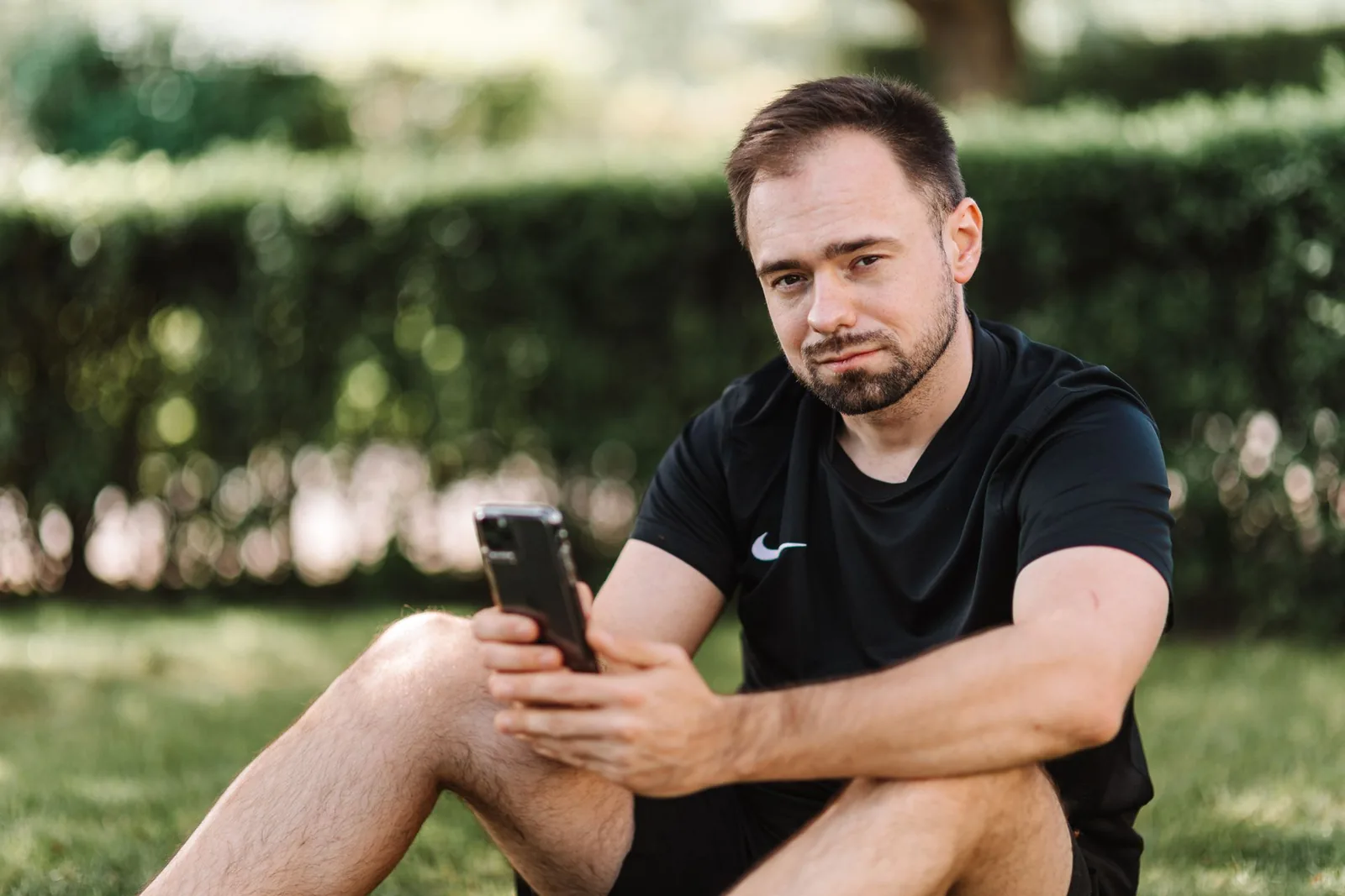 Mies istuu nurmikolla ja katsoo Ã¤lypuhelinta